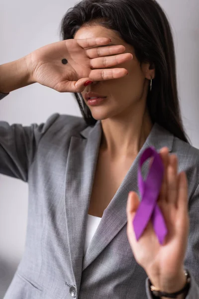 Selective focus of businesswoman with black dot on palm covering face and holding purple ribbon on grey, domestic violence concept — Stock Photo