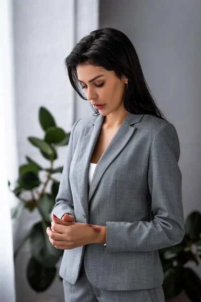 Mujer de negocios triste en blazer mirando moretones en la mano, concepto de violencia doméstica - foto de stock