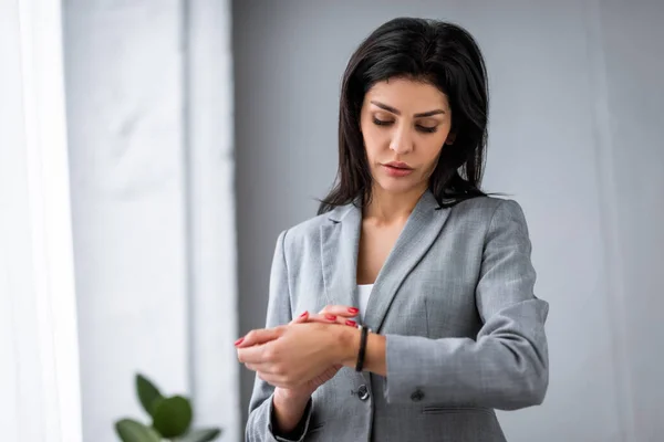 Triste donna d'affari con lividi a portata di mano guardando orologio, concetto di violenza domestica — Foto stock