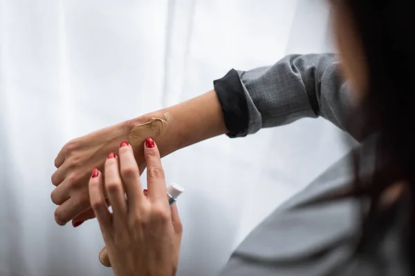 Enfoque selectivo de la mujer de negocios aplicando maquillaje fundación en la mano con moretones, concepto de violencia doméstica - foto de stock