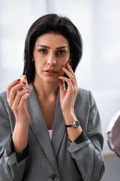 Businesswoman with bruise on face holding makeup sponge, domestic violence concept — Stock Photo
