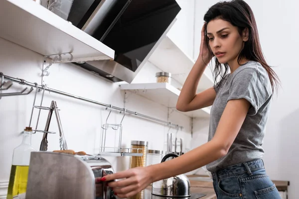 Frau mit Prellungen im Gesicht berührt Toaster in Küche, Konzept für häusliche Gewalt — Stockfoto