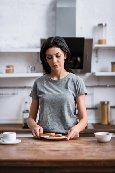 Selective focus of sad woman with bruise on face holding plate with toast bread, domestic violence concept — Stock Photo
