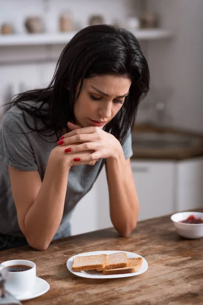Mujer molesta mirando el plato con pan tostado, concepto de violencia doméstica - foto de stock