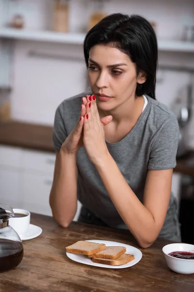 Selektiver Fokus der nachdenklichen Frau mit blauen Flecken im Gesicht beim Frühstück auf dem Tisch, Konzept häuslicher Gewalt — Stockfoto