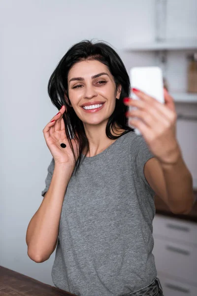 Selective focus of smiling woman with bruise on face and black dot on palm taking selfie, domestic violence concept — Stock Photo