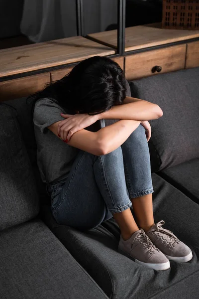 Mujer molesta cubriendo la cara mientras está sentada en el sofá, concepto de violencia doméstica - foto de stock