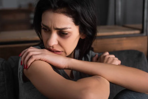 Mujer frustrada con moretones en la cara sentada en el sofá y mirando hacia otro lado, concepto de violencia doméstica — Stock Photo