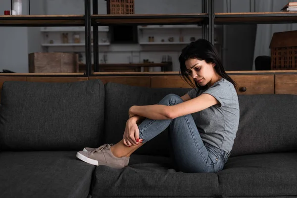 Разочарованная женщина с синяком на лице, сидящая на диване в гостиной, концепция домашнего насилия — стоковое фото