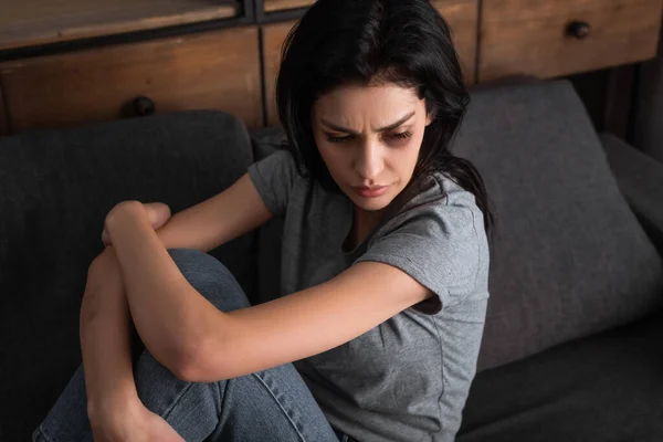 Розчарована жінка з синцем на обличчі сидить на дивані у вітальні, концепція домашнього насильства — стокове фото