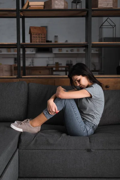 Donna depressa con lividi sul viso seduta sul divano in soggiorno, concetto di violenza domestica — Foto stock
