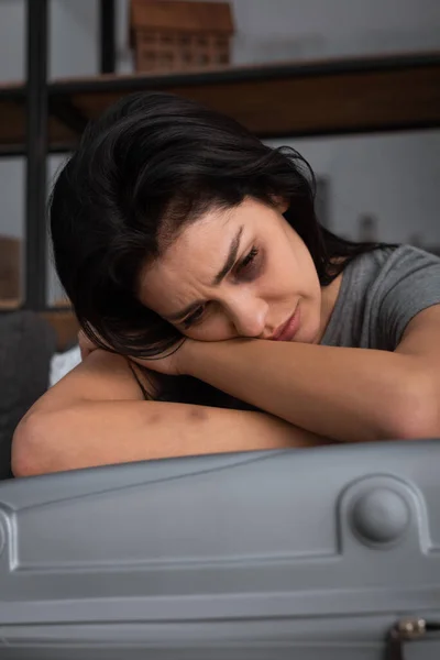 Депрессивная женщина с синяком на лице плачет рядом с чемоданом, концепция домашнего насилия — стоковое фото