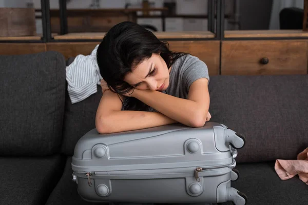 Депрессивная женщина с синяком на лице, сидя на диване рядом с чемоданом, концепция домашнего насилия — стоковое фото