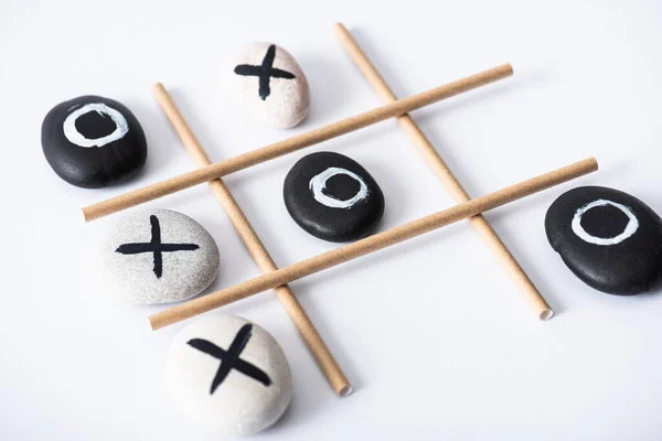 Tic tac toe game with grid made of paper tubes, and pebbles marked with naughts and crosses on white surface — Stock Photo