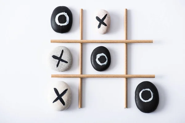 Top view of tic tac toe game with grid made of paper tubes, and pebbles marked with naughts and crosses on white surface — Stock Photo