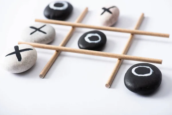 Selective focus of tic tac toe game with grid made of paper tubes, and pebbles marked with naughts and crosses on white surface — Stock Photo