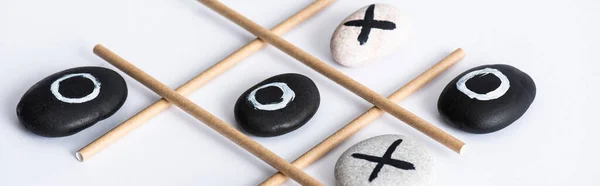 Panoramic shot of tic tac toe game with grid made of paper tubes, and pebbles marked with naughts and crosses on white surface — Stock Photo