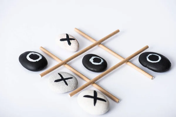Tic tac toe game with grid made of paper tubes, and pebbles marked with naughts and crosses on white surface — Stock Photo