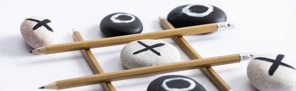 Panoramic shot of tic tac toe game with grid made of pencils, and pebbles marked with naughts and crosses on white surface — Stock Photo