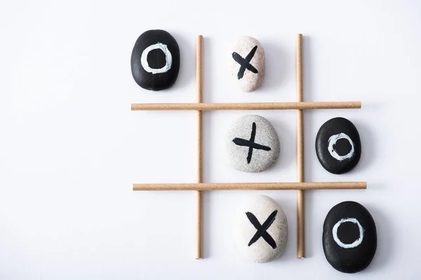Top view of tic tac toe game with grid made of paper tubes, and pebbles marked with crosses and naughts on white surface — Stock Photo