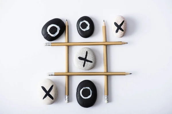 Top view of tic tac toe game with grid made of pencils, and pebbles marked with crosses and naughts on white surface — Stock Photo