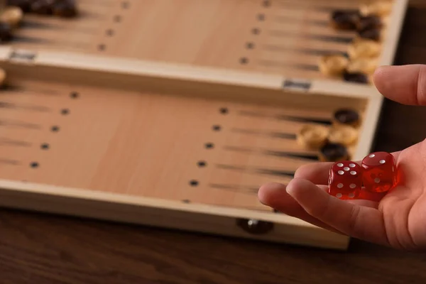 KYIV, UCRANIA - 30 de enero de 2019: vista parcial del hombre sosteniendo el par de dados cerca del tablero de backgammon con damas en la mesa de madera - foto de stock