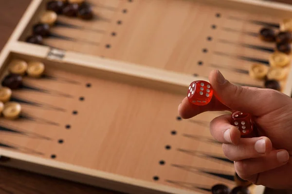 KYIV, UKRAINE - JANUARY 30, 2019: cropped view of man holding dice pair near backgammon board with checkers — Stock Photo