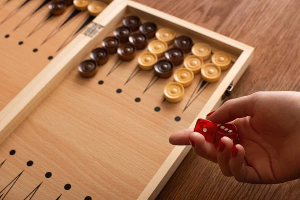 KYIV, UCRANIA - 30 de enero de 2019: vista recortada de una mujer sosteniendo un par de dados cerca del tablero de backgammon con damas en una mesa de madera - foto de stock