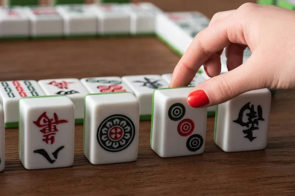 KYIV, UKRAINE - 30 JANVIER 2019 : vue partielle de la femme prenant une tuile de jeu de mahjong de la table en bois — Photo de stock