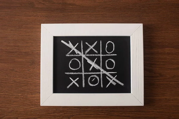 Vue du haut du jeu tic tac toe sur tableau noir avec rangée rayée de croix sur surface en bois — Photo de stock