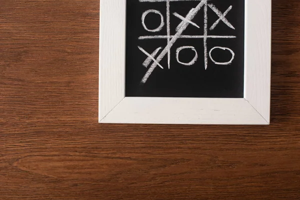 Top view of tic tac toe game on blackboard with crossed out row of crosses on wooden surface — Stock Photo