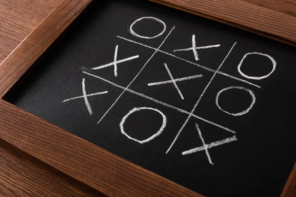 Tic tac toe game on blackboard with chalk grid, naughts and crosses on wooden surface — Stock Photo