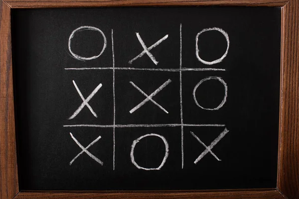 Top view of tic tac toe game on blackboard with chalk grid, naughts and crosses — Stock Photo
