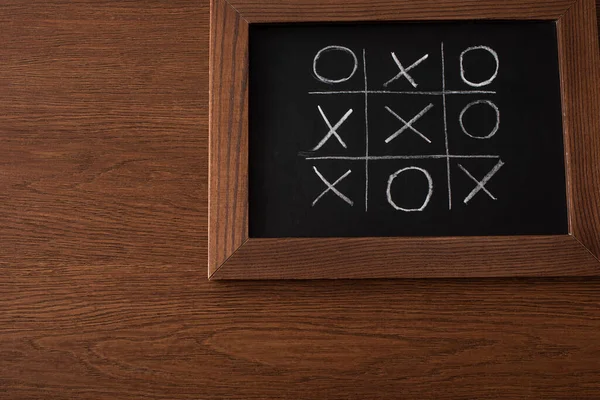 Vue de dessus du jeu tic tac toe sur tableau noir avec grille de craie, nausées et croix sur surface en bois — Photo de stock