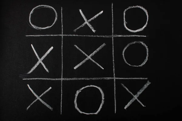 Top view of tic tac toe game on blackboard with chalk grid, naughts and crosses — Stock Photo