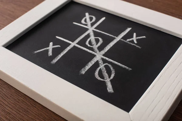 Tic tac toe game on chalkboard in white frame with crossed out row of naughts — Stock Photo