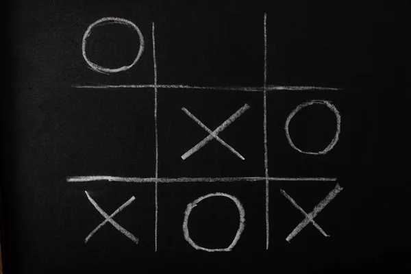 Top view of tic tac toe game on blackboard with chalk grid, naughts and crosses — Stock Photo