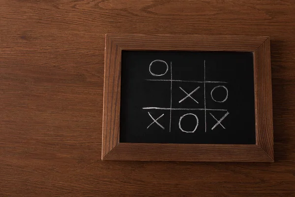 Top view of tic tac toe game on blackboard with chalk grid, naughts and crosses on wooden surface — Stock Photo