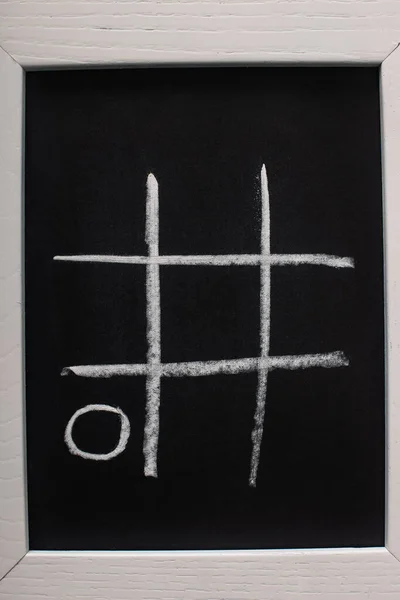 Top view of tic tac toe game on blackboard with chalk grid and naught on wooden surface — Stock Photo
