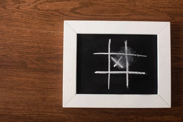 Top view of tic tac toe game on blackboard with chalk grid and cross on wooden surface — Stock Photo