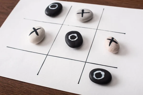 Tic tac toe jeu sur papier blanc avec des cailloux marqués avec des nausées et des croix sur la surface en bois — Photo de stock