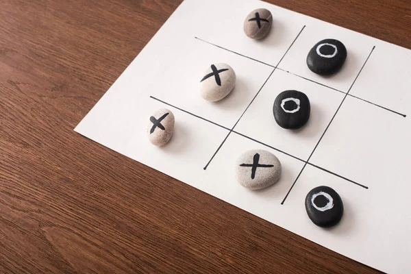 Tic tac toe game on white paper with pebbles marked with naughts and crosses on wooden surface — Stock Photo