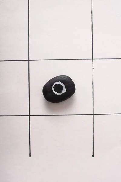 Top view of tic tac toe game with black pubble marked with naught on white paper — Stock Photo