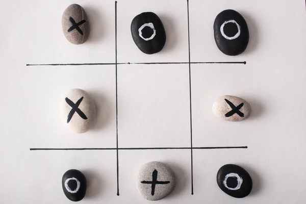 Vista dall'alto del gioco tic tac toe con pietre segnate con nulla e croci su carta bianca — Foto stock