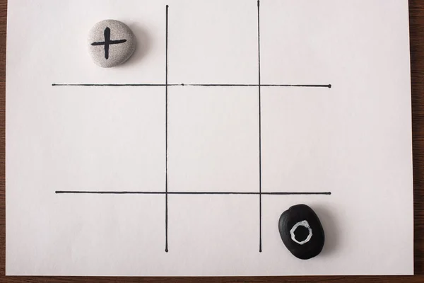 Draufsicht auf Tic Tac Toe Spiel mit Steinen, die mit Nichts und Kreuz auf weißer Oberfläche markiert sind — Stockfoto