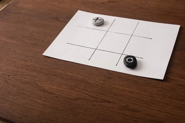 Tic Tac Toe Spiel auf weißem Papier mit Kieselsteinen, die mit Nichts und Kreuz auf Holzoberfläche markiert sind — Stockfoto