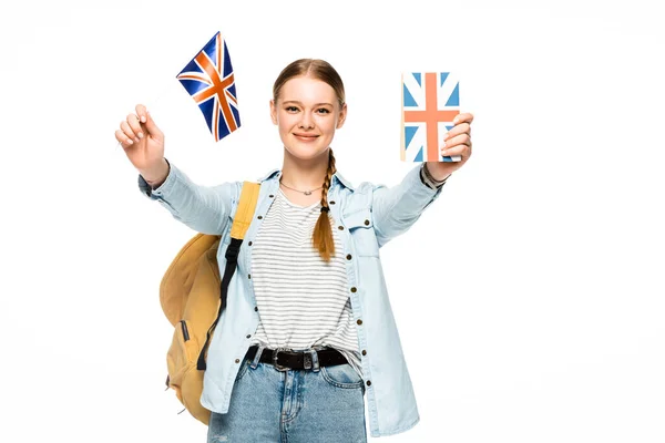 Sonriente bonita estudiante con mochila mostrando libro y bandera británica aislado en blanco - foto de stock