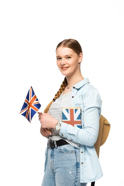 Sorrindo estudante bonita com mochila segurando livro e bandeira britânica isolada no branco — Fotografia de Stock