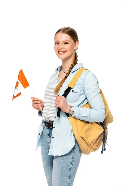 Sonriente bonita estudiante con mochila sosteniendo bandera canadiense aislado en blanco - foto de stock