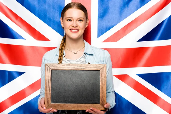Sourire jolie fille avec tresse tenant tableau blanc sur fond drapeau britannique — Photo de stock